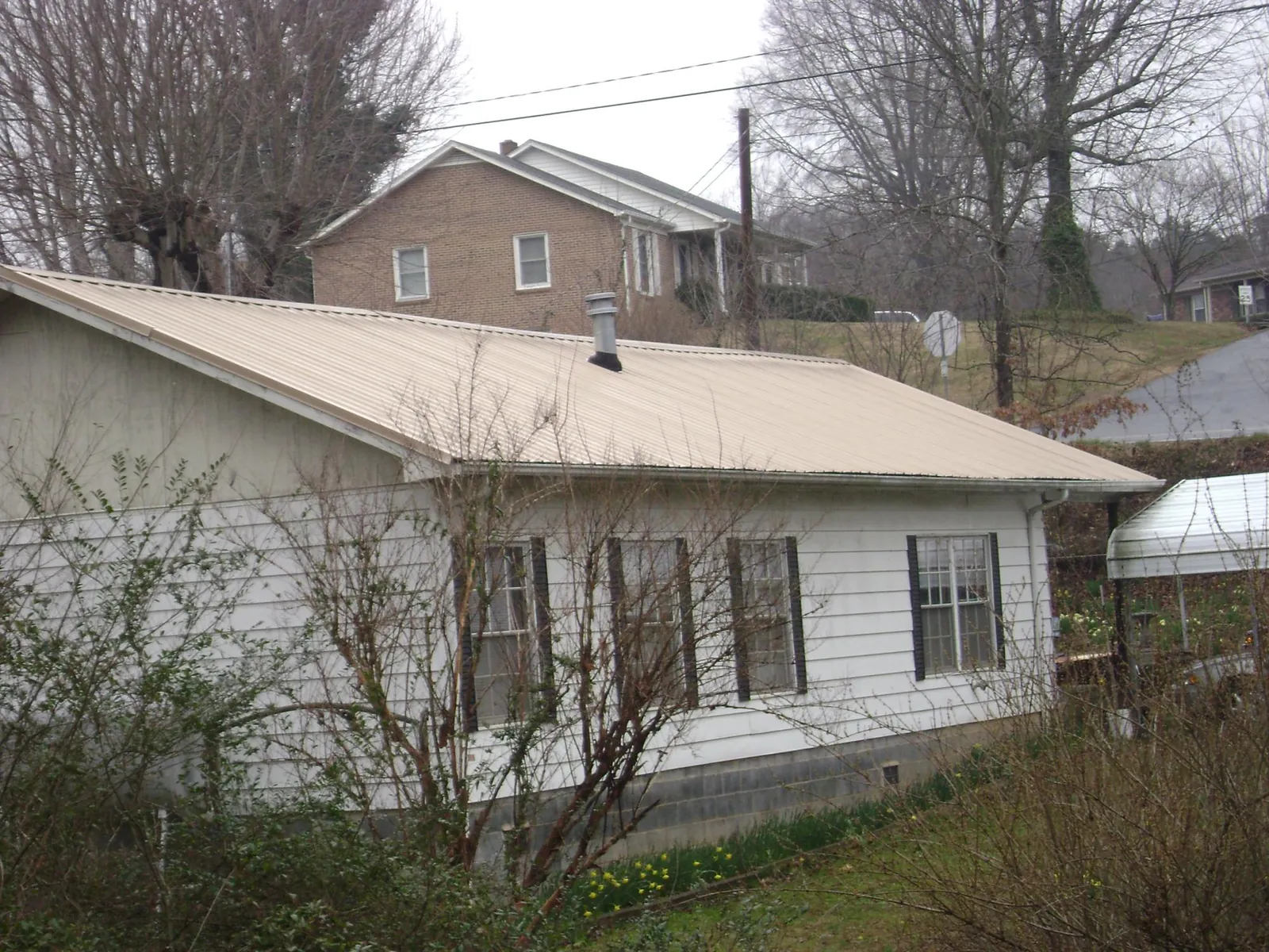 Tan metal roof on a white sided house set into a hillside — Commercial Roofing by Roofing Brothers in Union